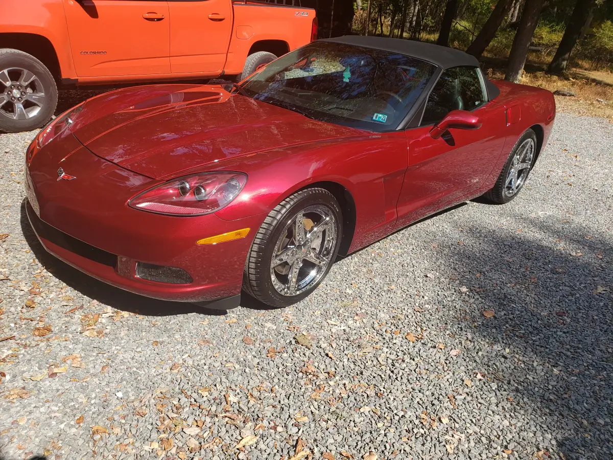 Dark red Corvette convertible with black top parked next to an orange pickup truck