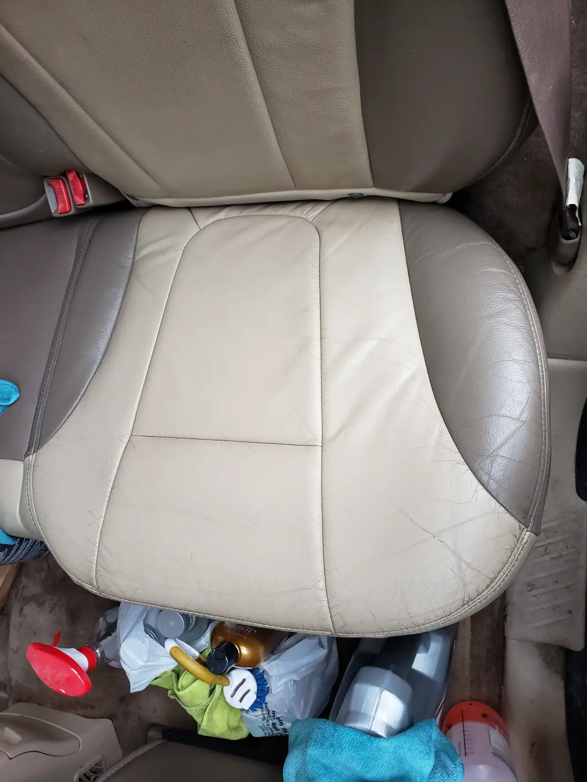 Tan leather rear seat with cleaning supplies and rags on the floor during detailing