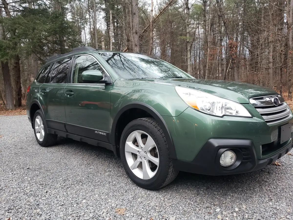 Green Subaru Outback front three-quarter view freshly detailed in a wooded driveway
