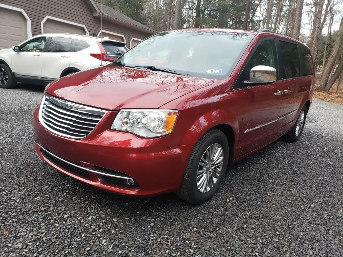 Dark red Chrysler Town and Country minivan parked in a wooded gravel driveway