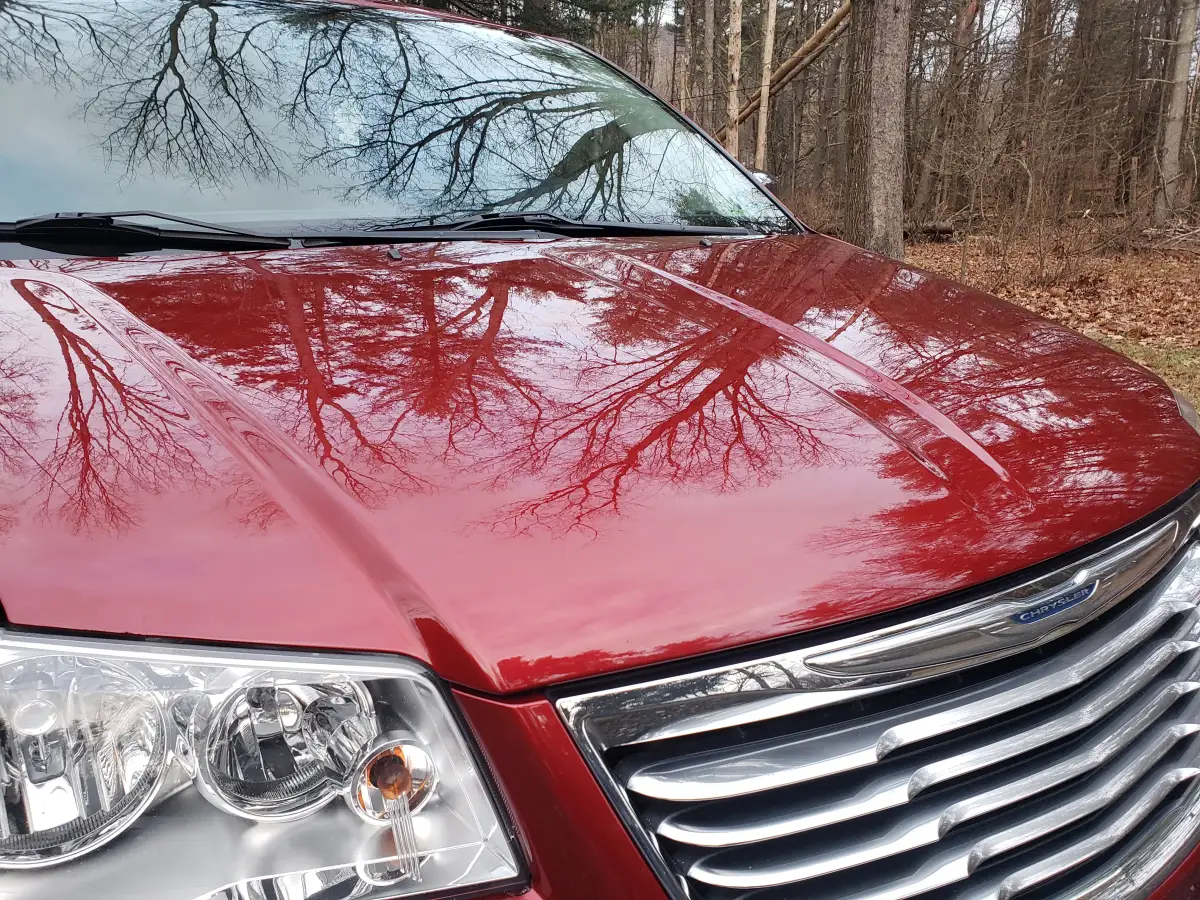 Glossy red Chrysler minivan hood reflecting bare winter trees after ceramic coating