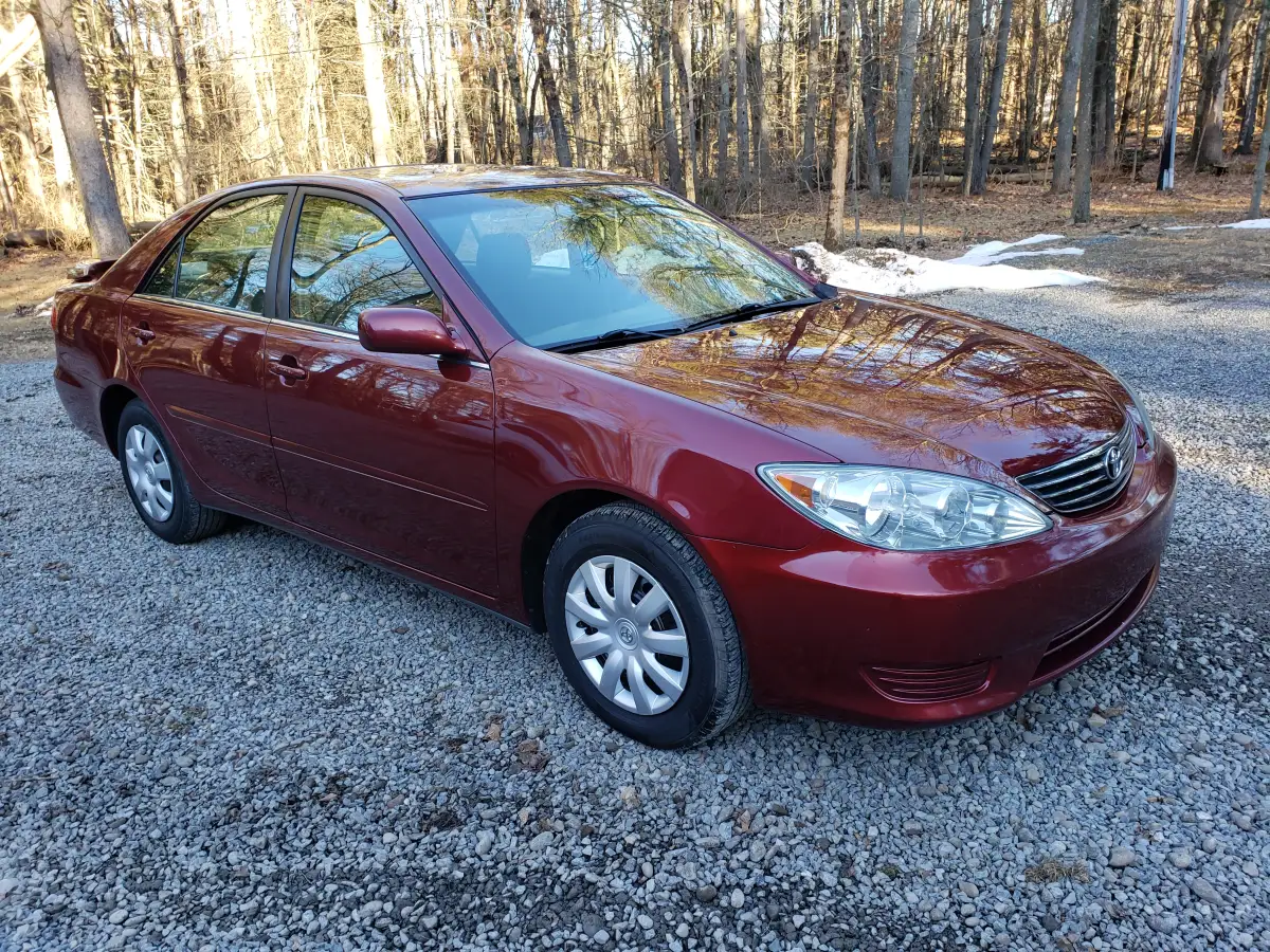 Clean maroon Toyota Camry parked on a gravel driveway in the woods