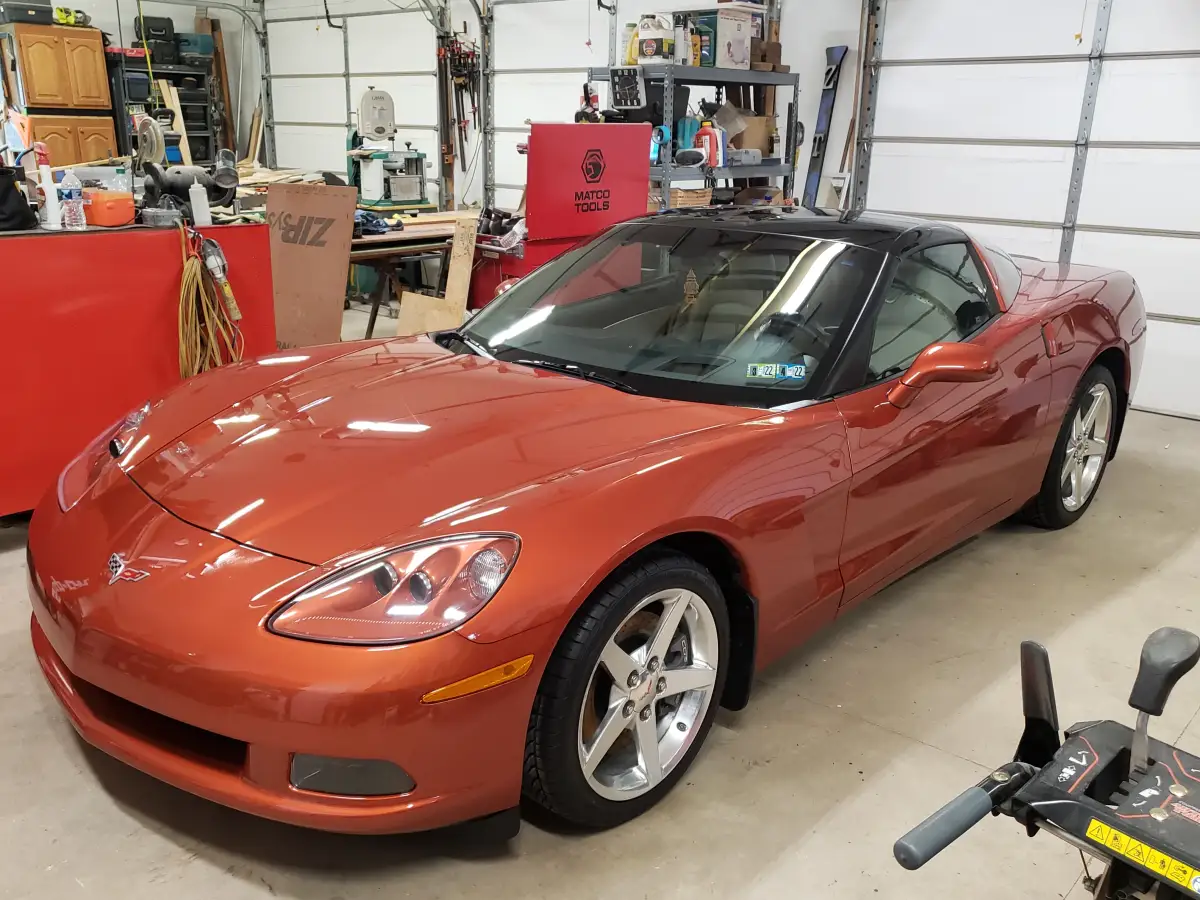 Orange Chevrolet Corvette with black roof detailed in a home garage