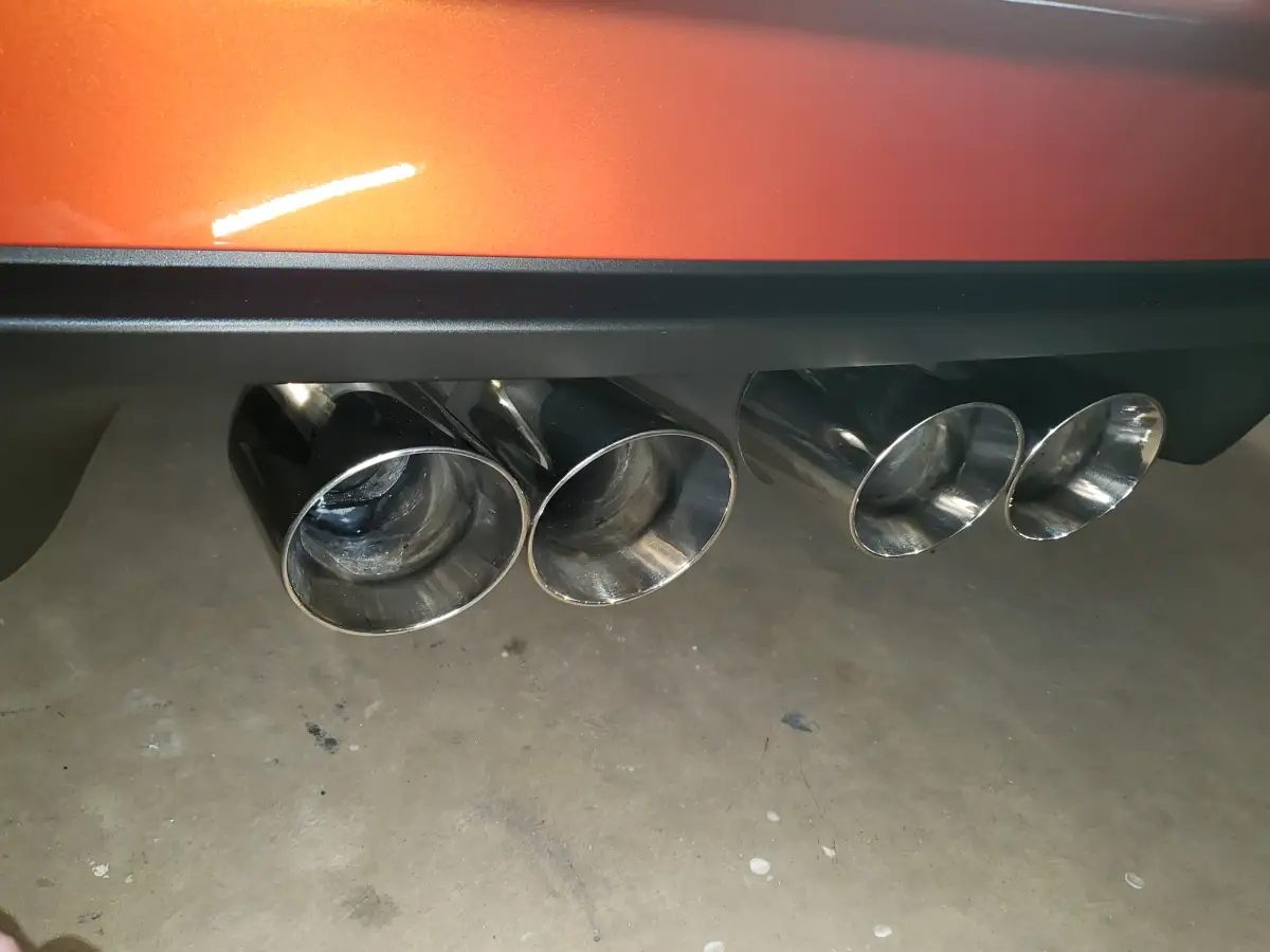 Close-up of polished quad chrome exhaust tips on an orange Corvette