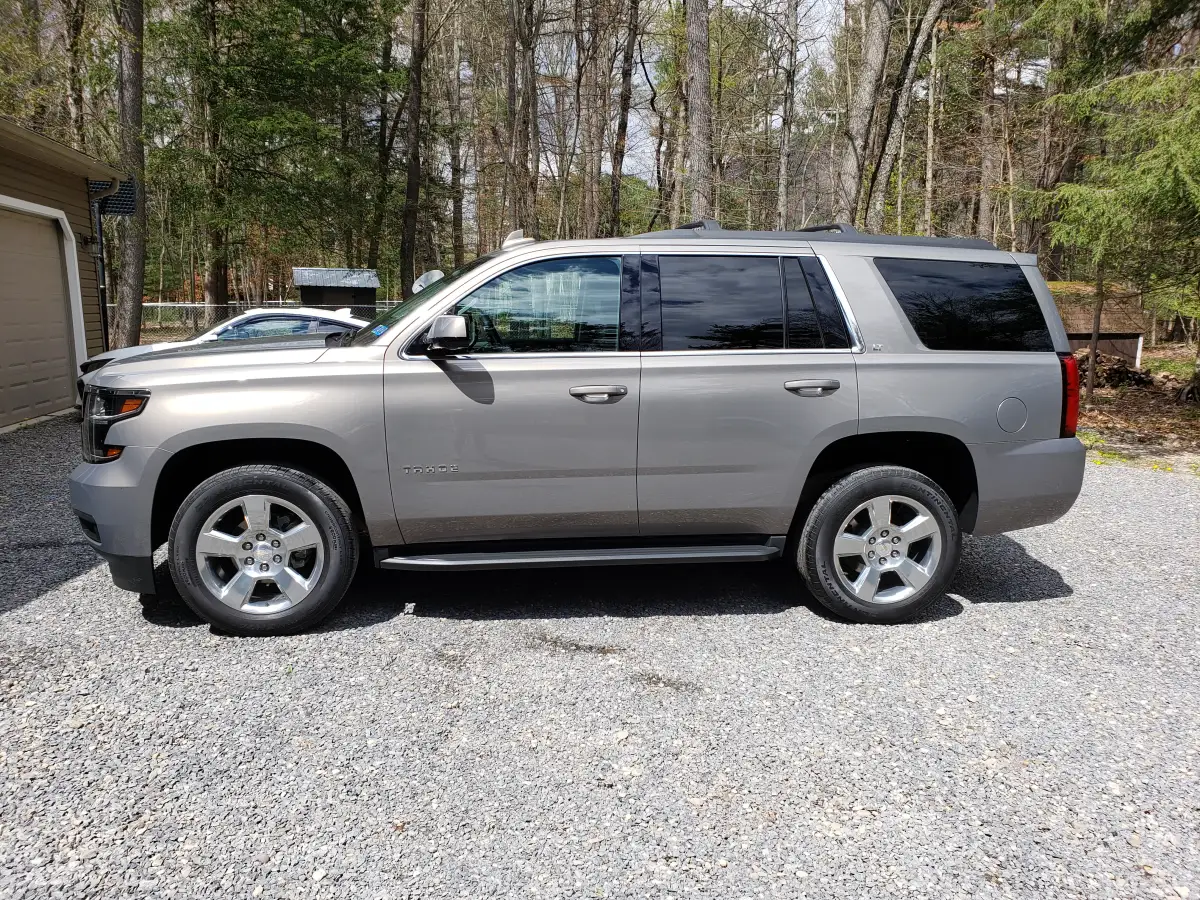 Clean gray Chevrolet Tahoe parked in a gravel driveway surrounded by trees