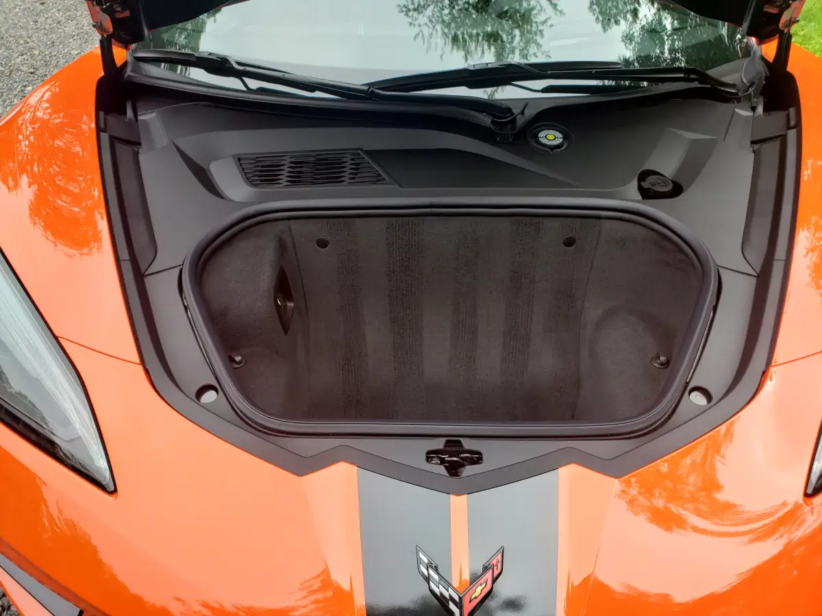 Detailed front trunk and engine compartment of an orange Corvette with hood open