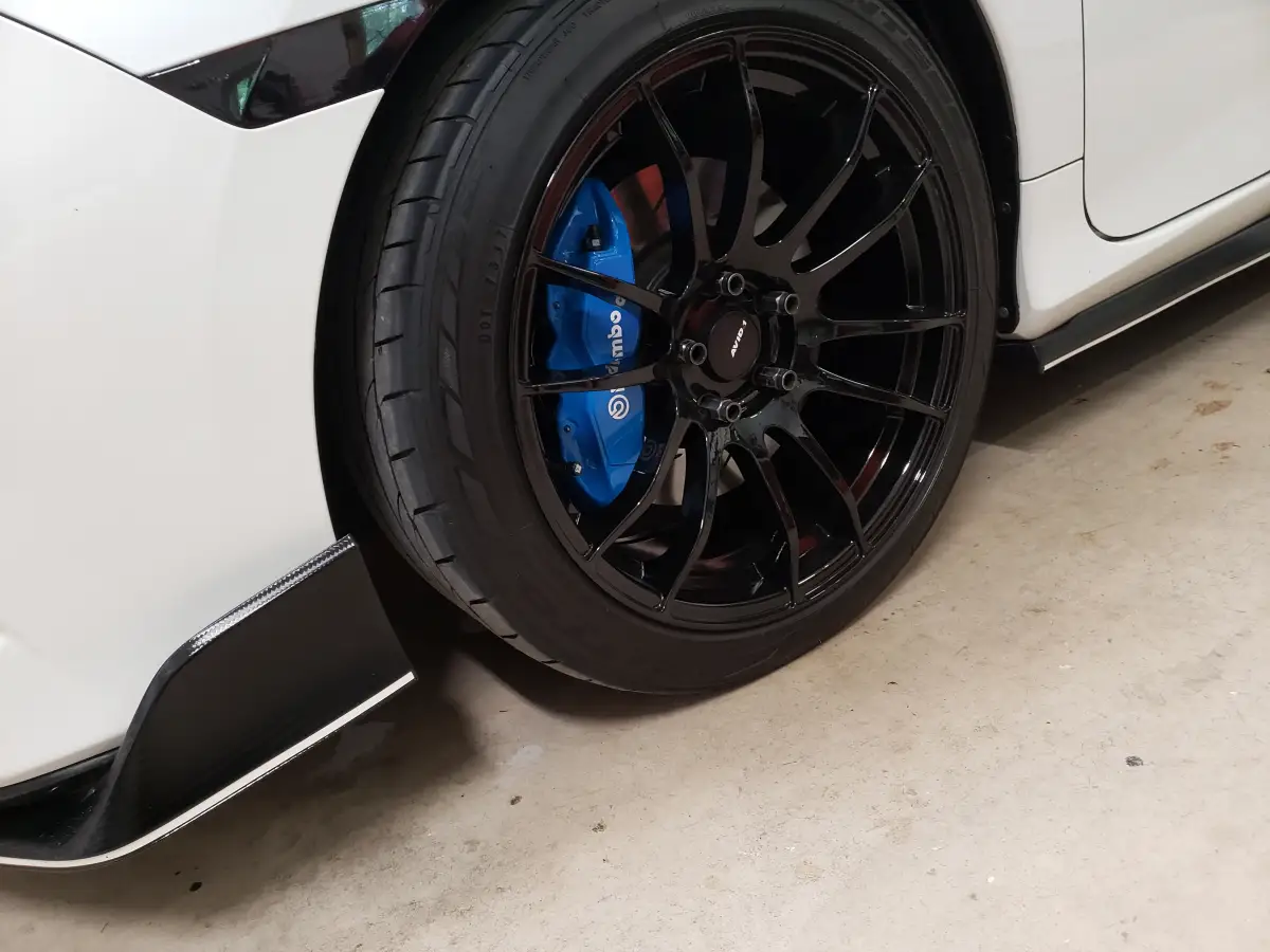 Close-up of a glossy black wheel with blue Brembo brake caliper on a white car