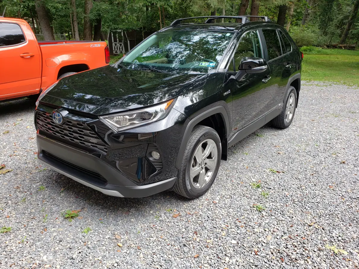 Detailed black Toyota RAV4 Hybrid SUV parked on a gravel driveway next to an orange truck