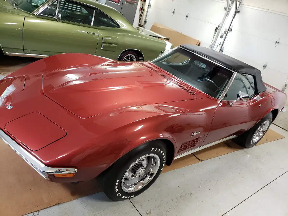 Detailed dark red 1970s Corvette Stingray convertible parked next to a classic green muscle car