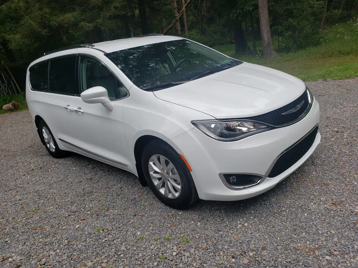 Freshly washed white Chrysler Pacifica minivan parked on a gravel driveway near trees