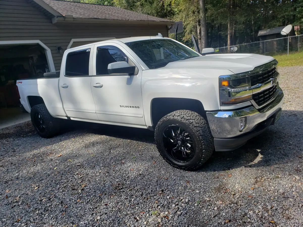 White lifted Chevrolet Silverado pickup truck with black wheels parked on gravel after detailing