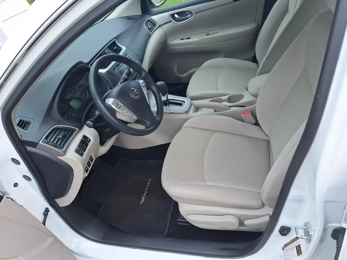 Clean beige cloth driver seat, dashboard and steering wheel of a white Nissan Sentra after interior detailing