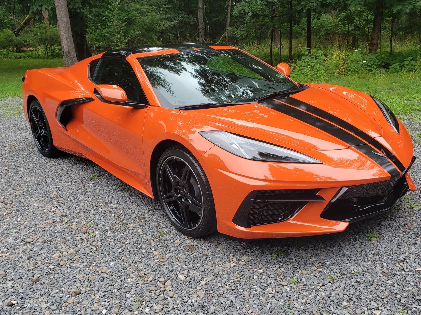 Freshly detailed orange Chevrolet Corvette with black racing stripes parked on gravel