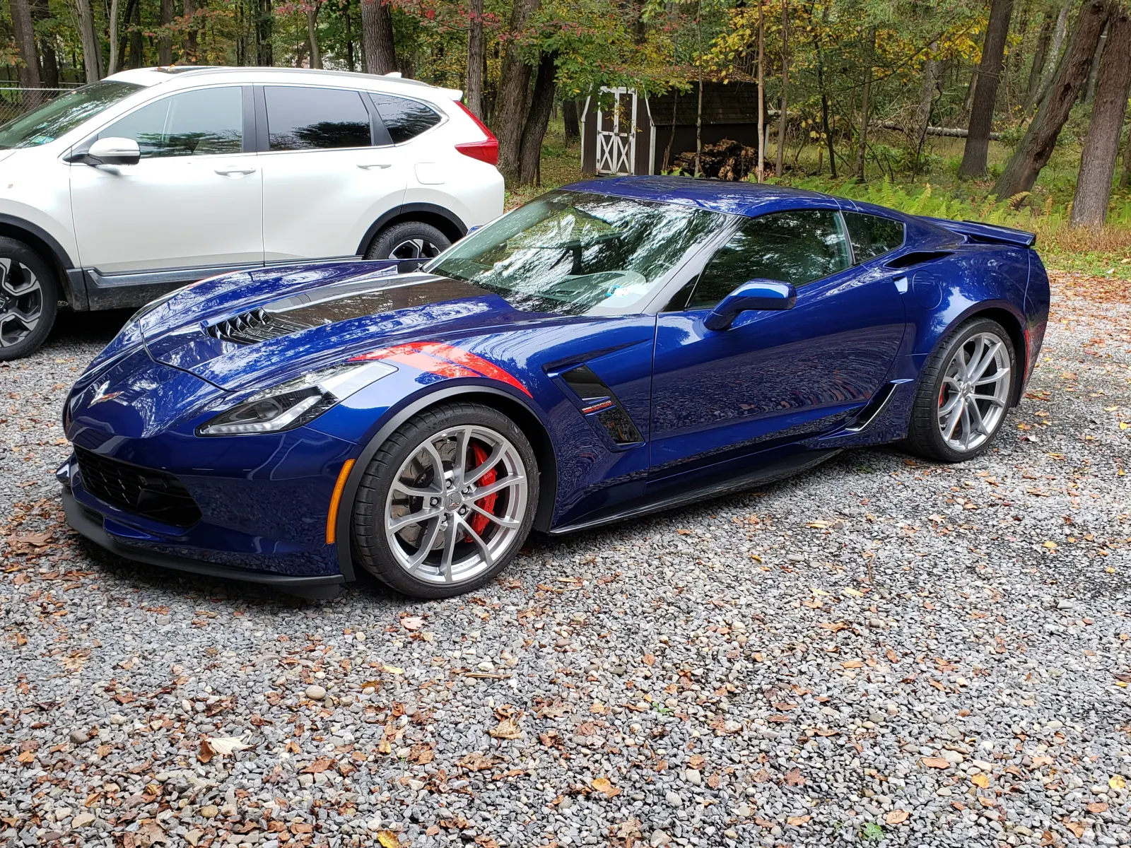 Blue Chevrolet Corvette Grand Sport with polished wheels and red brake calipers on a gravel lot
